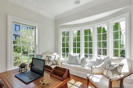 Home office with desk, laptop, chairs, and large bay windows overlooking a green yard.