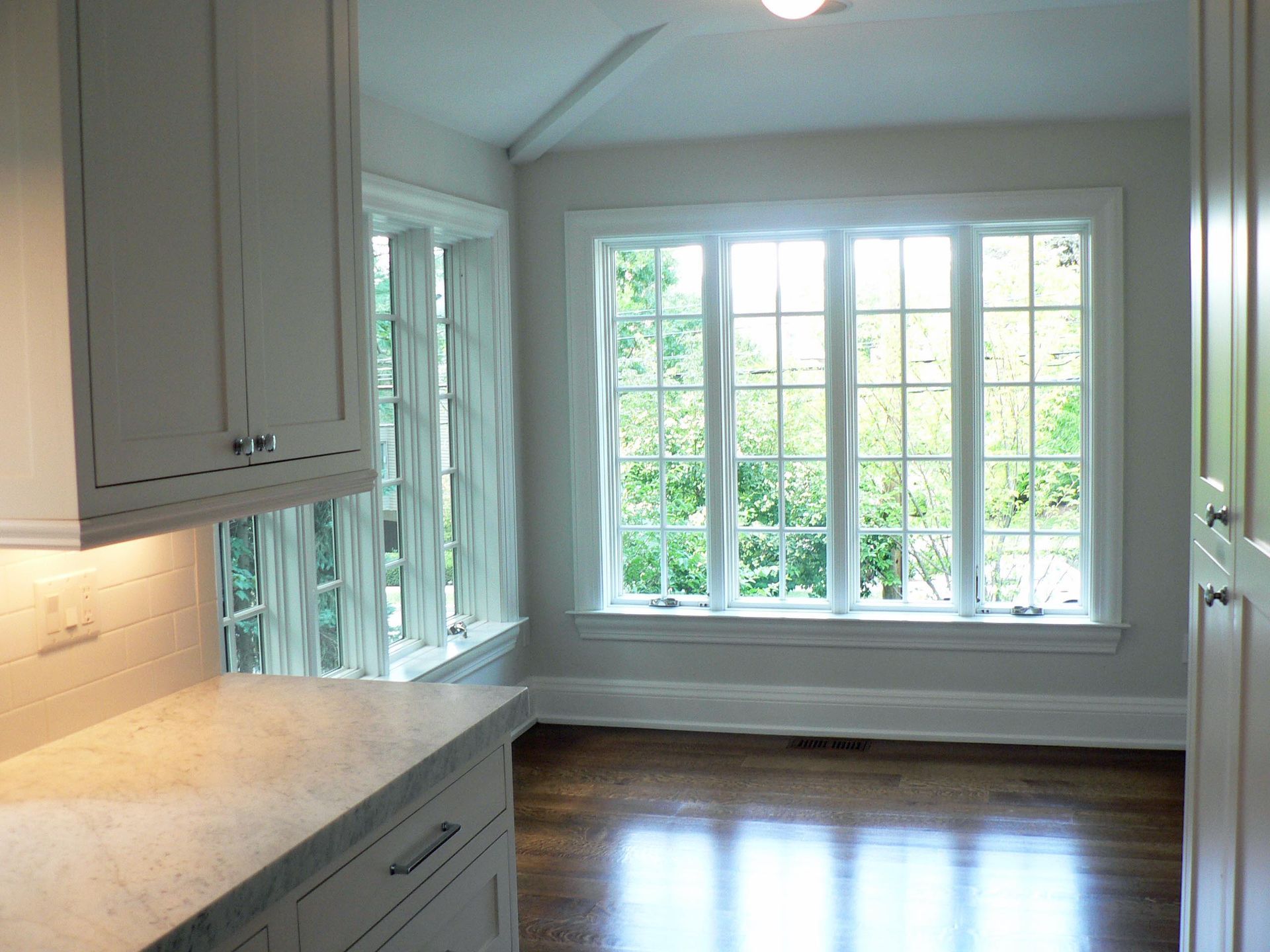 Kitchen with white cabinets, large windows, and a wood floor.
