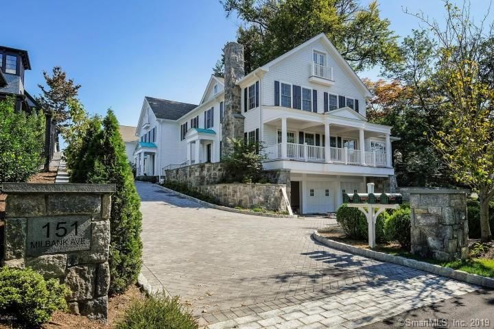 White house with stone facade, driveway, and mailbox; trees in the background.