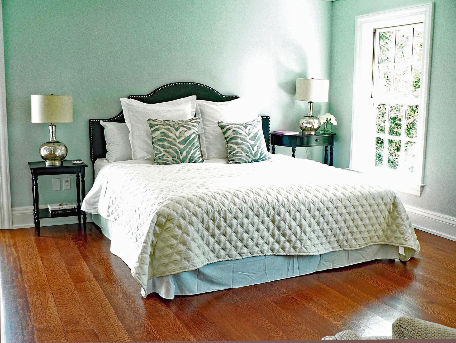 Bedroom with wooden floors, mint walls, bed with white quilt, two nightstands with lamps, and a window.