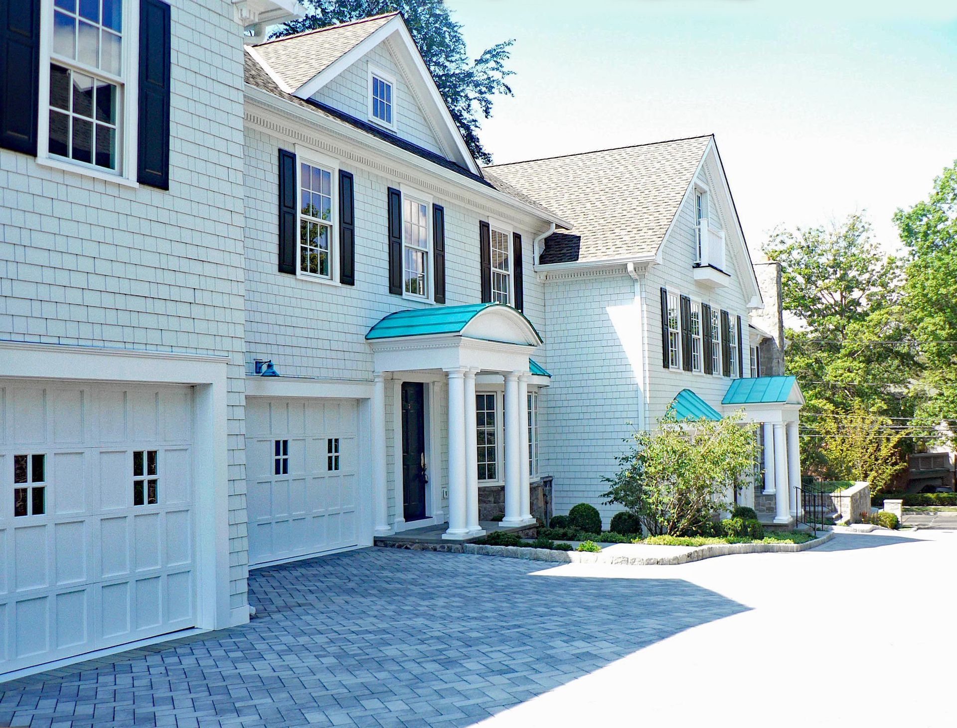 White house with black shutters, blue accents, and a brick driveway.