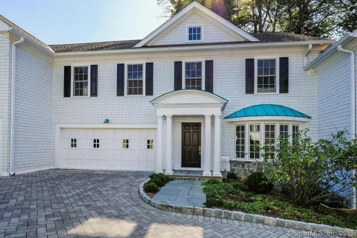 White house with black shutters, blue accents, and a brick driveway.