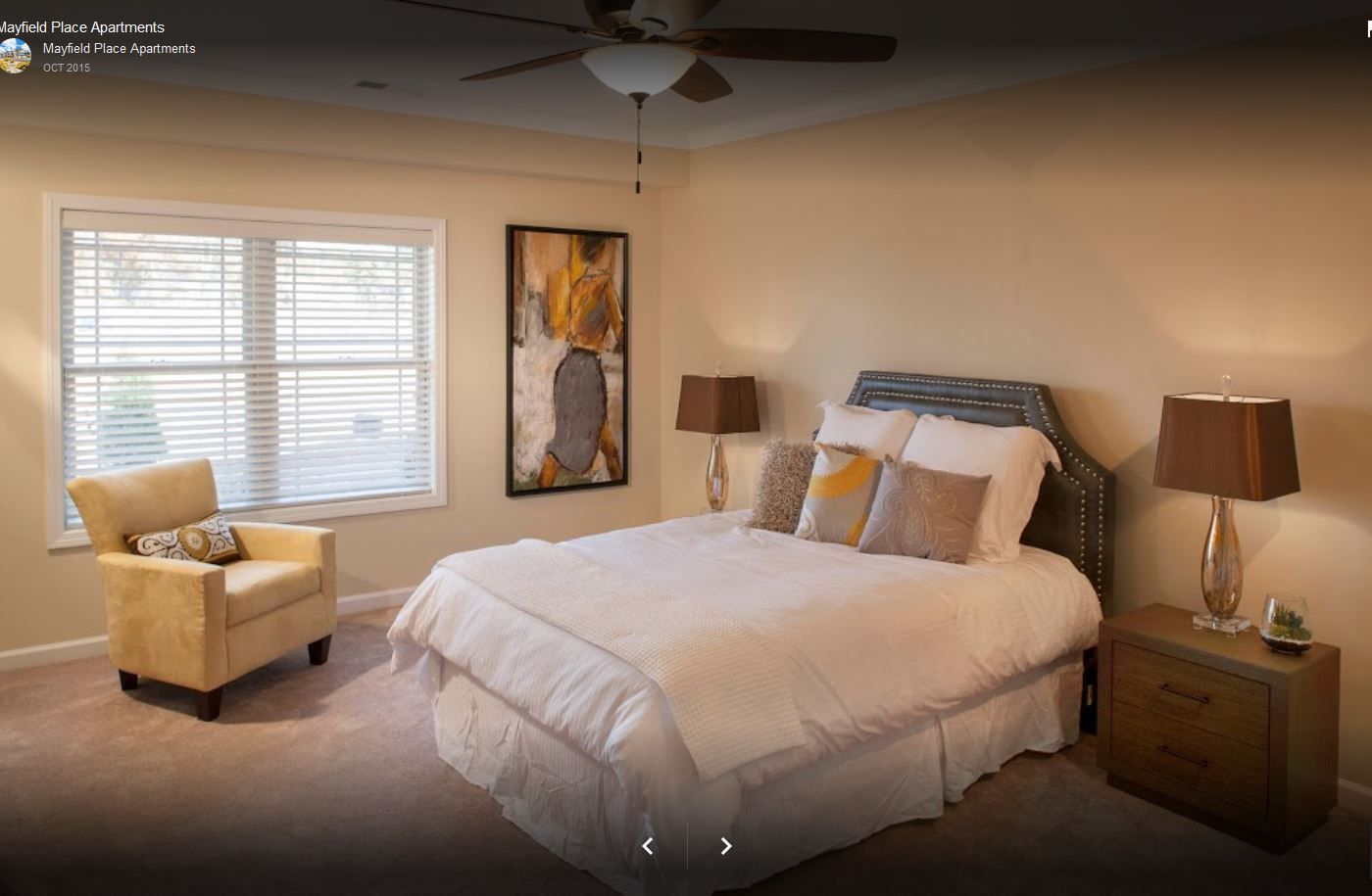 Bedroom with a bed, nightstand, armchair, window with blinds, artwork, and ceiling fan.