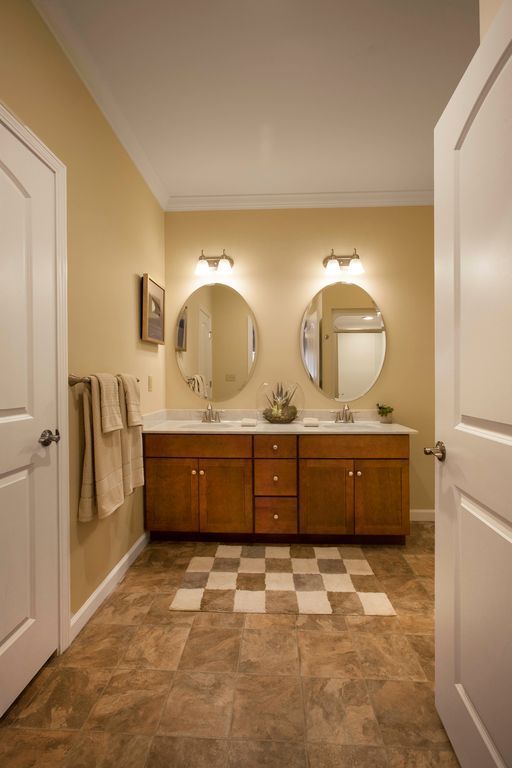Bathroom with double vanity, two round mirrors, beige walls, and brown tile floor.