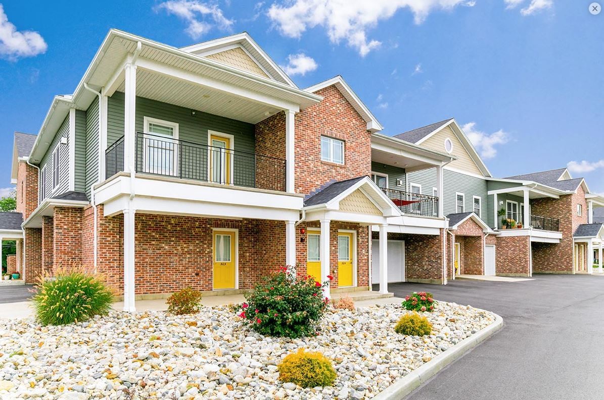 Multi-unit apartment building with brick and green siding, yellow doors, and white balconies.