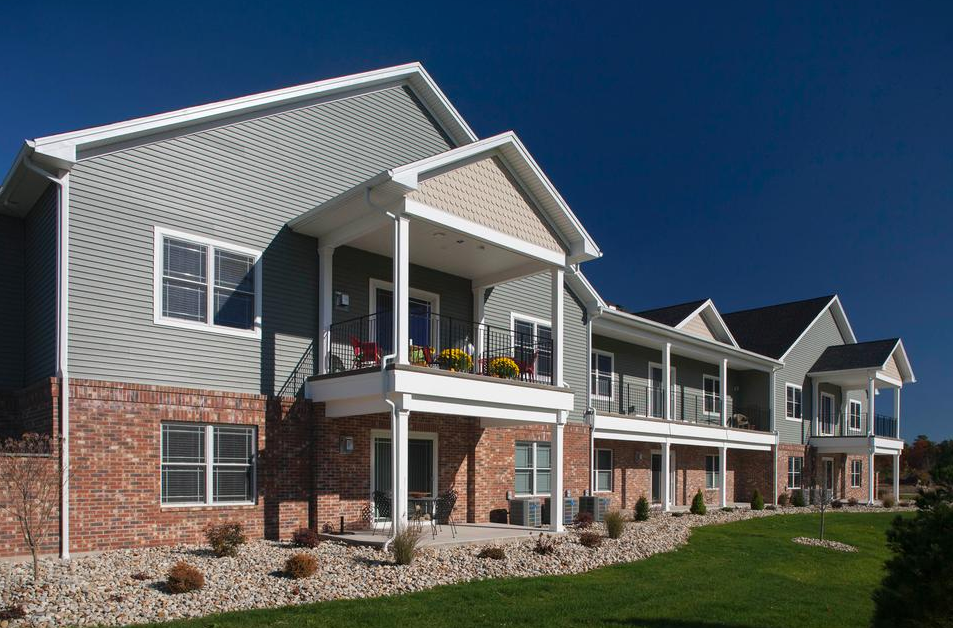 Apartment buildings with green siding, brick accents, balconies, and blue sky.