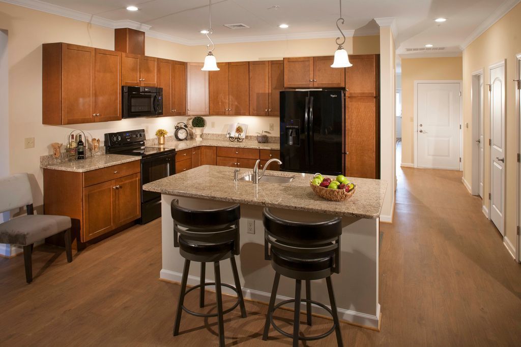 Kitchen with wooden cabinets, black appliances, granite countertops, and a central island with stools.
