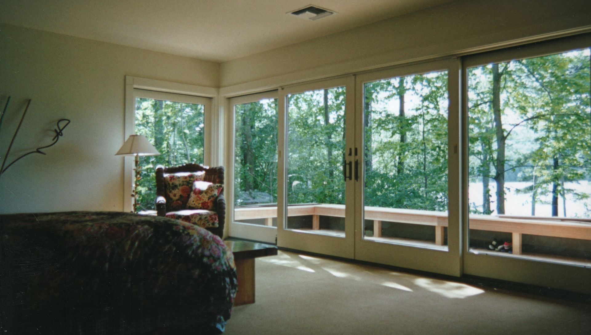 Room with large windows overlooking trees. A chair and bed are in the room.