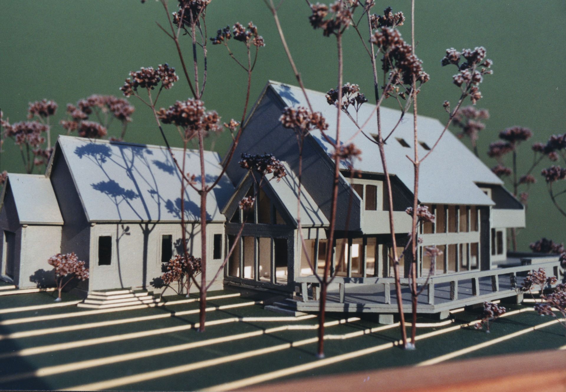 Architectural model of a house and separate structure, with a deck. Trees are interspersed in the foreground.