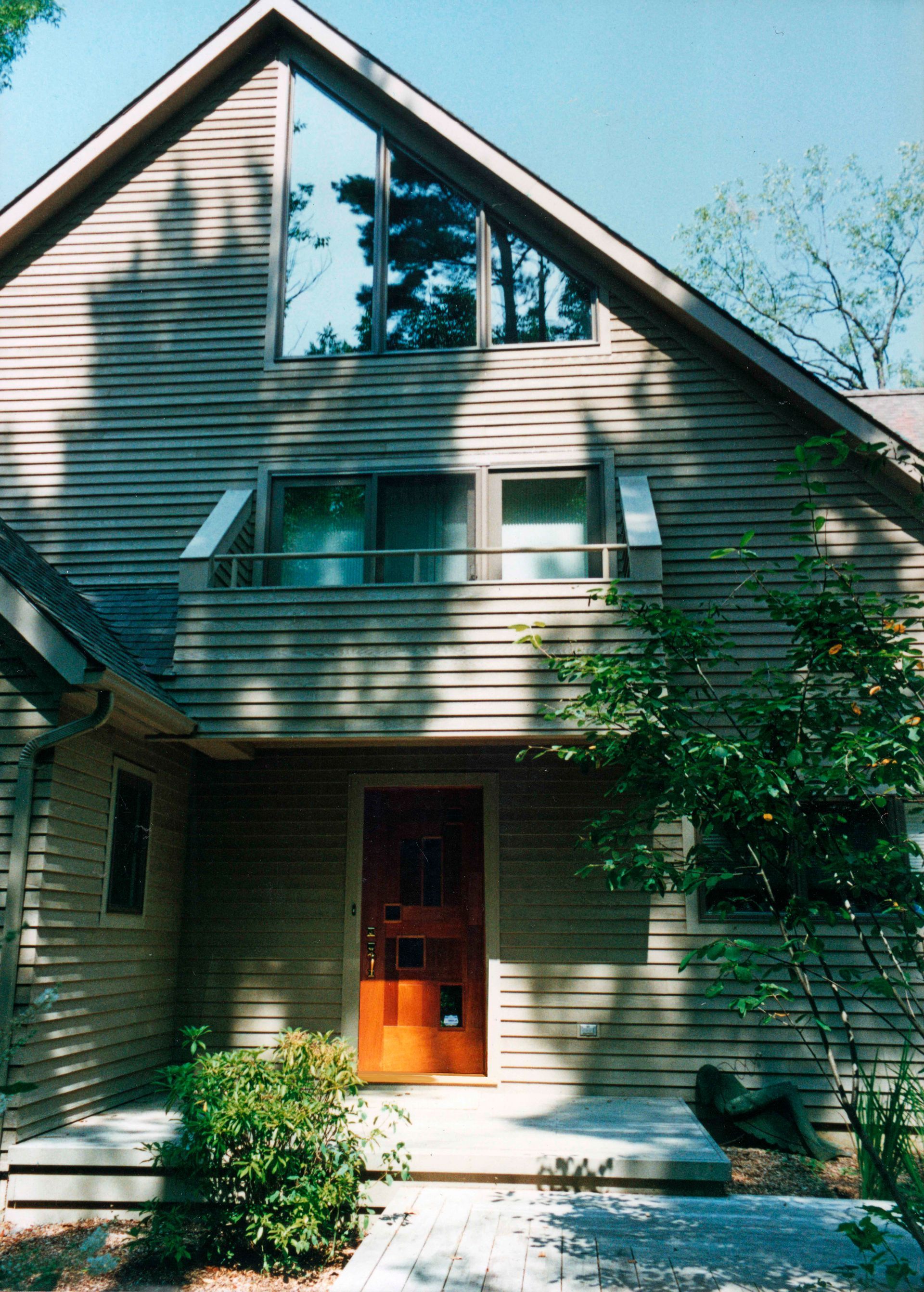 Brown wooden house with triangular window, front door, and small balcony.