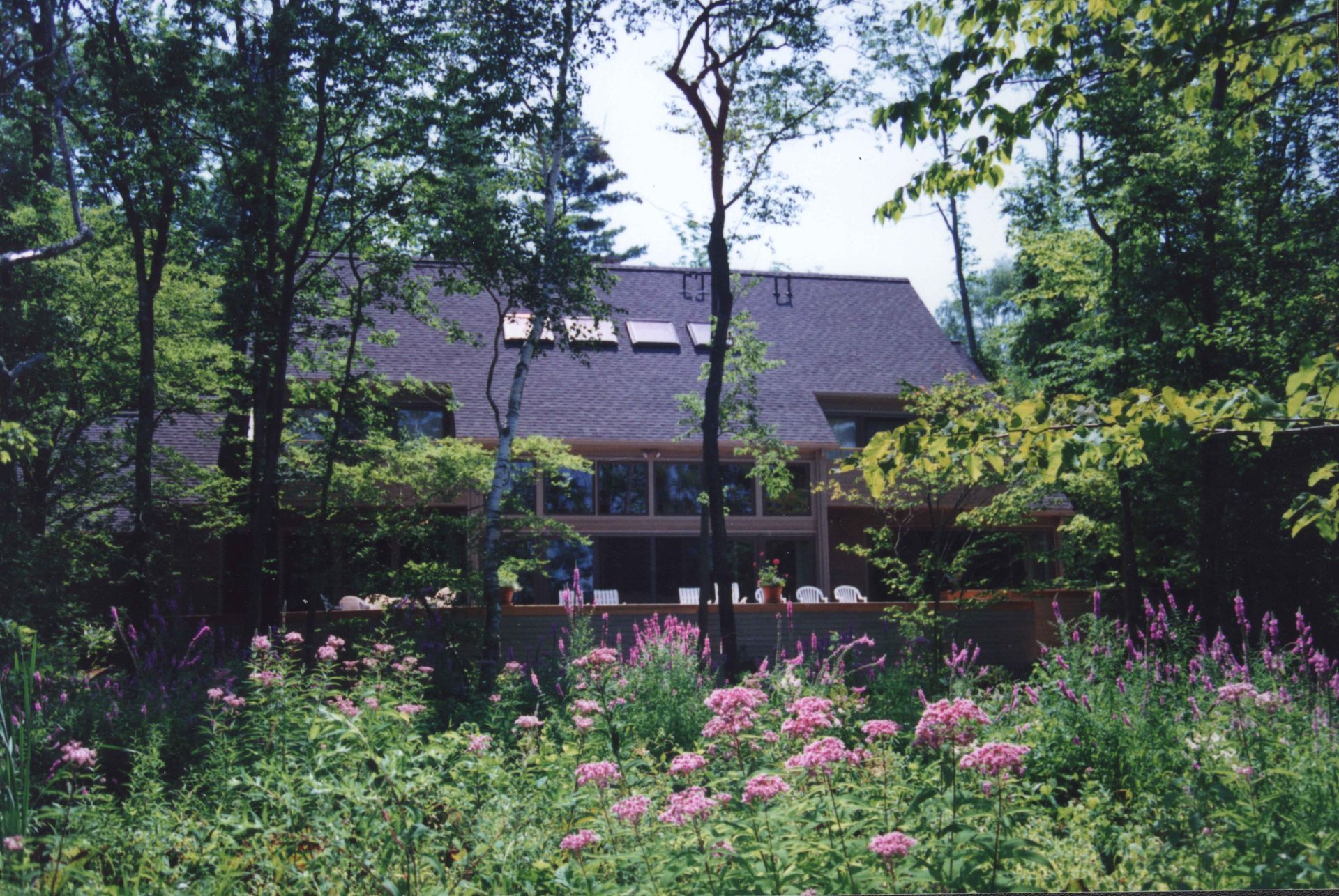 House nestled in trees, with a pink flower garden in front.