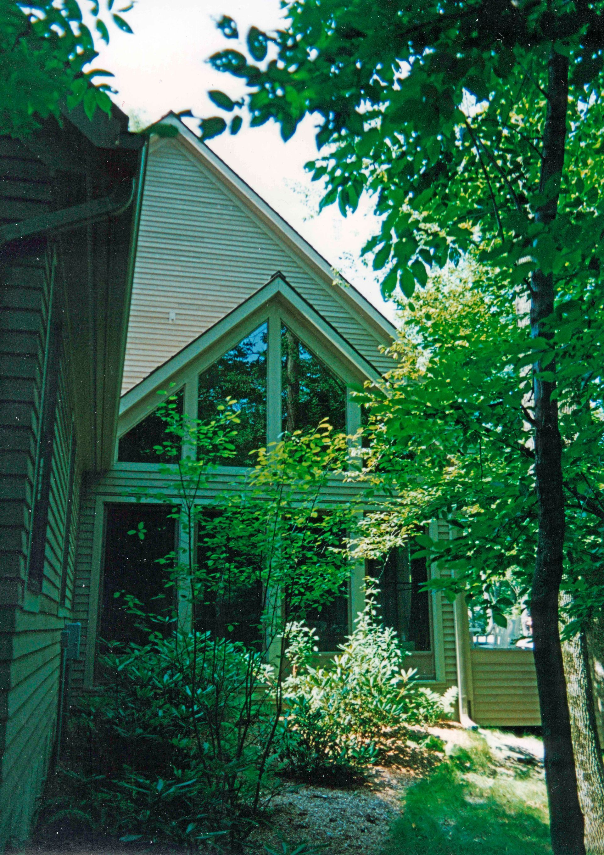 A-frame house with large windows, surrounded by trees and greenery.