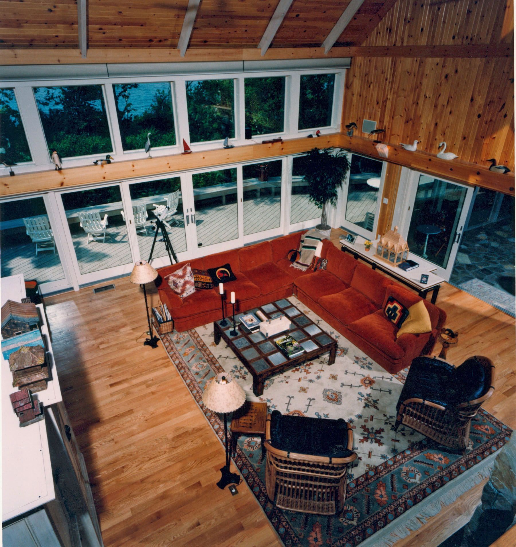 High-angle view of a large living room with a red sectional, windows, and wood paneling.