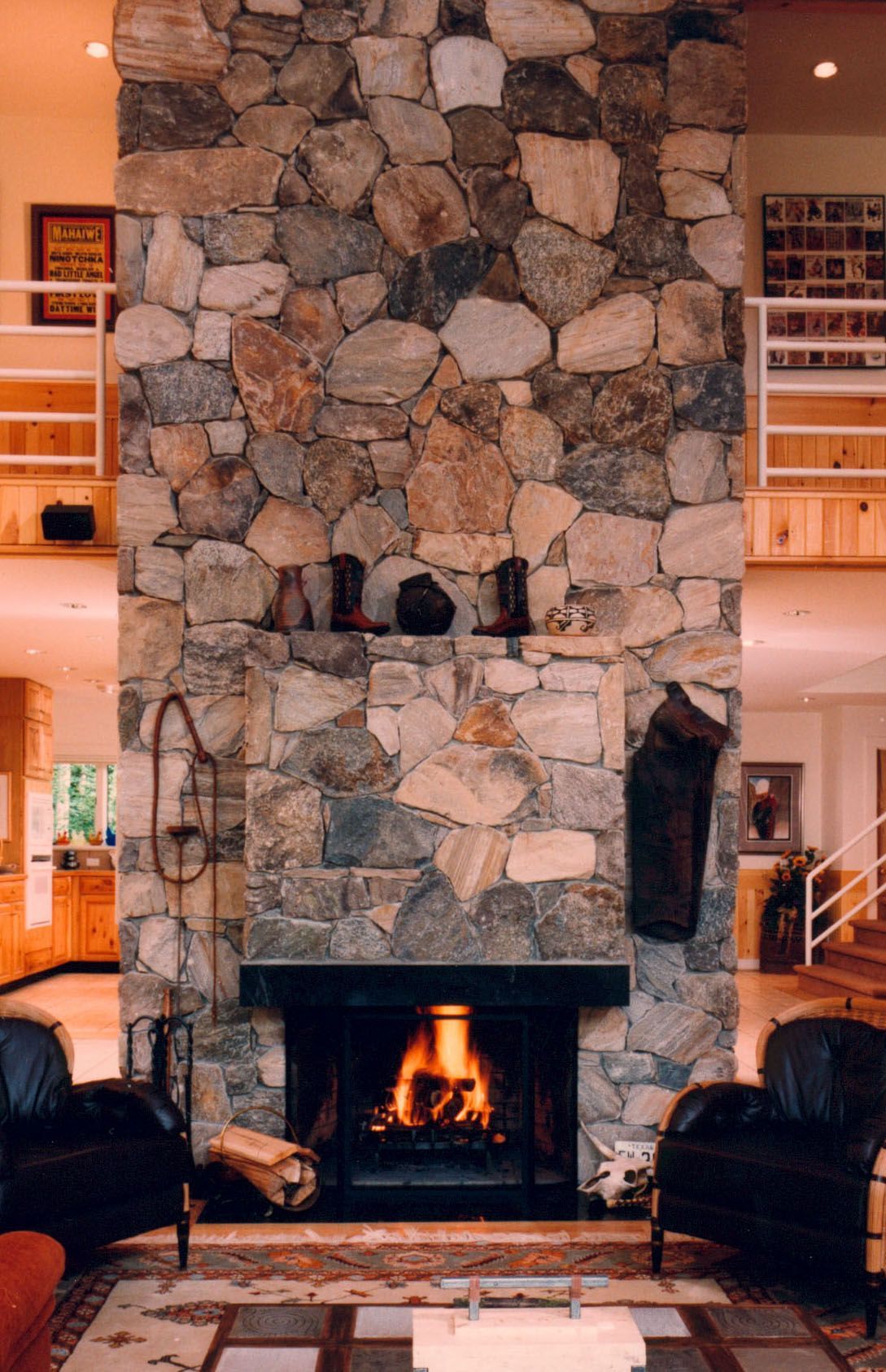 Stone fireplace with fire, flanked by black leather chairs. Stocking hangs on the right.
