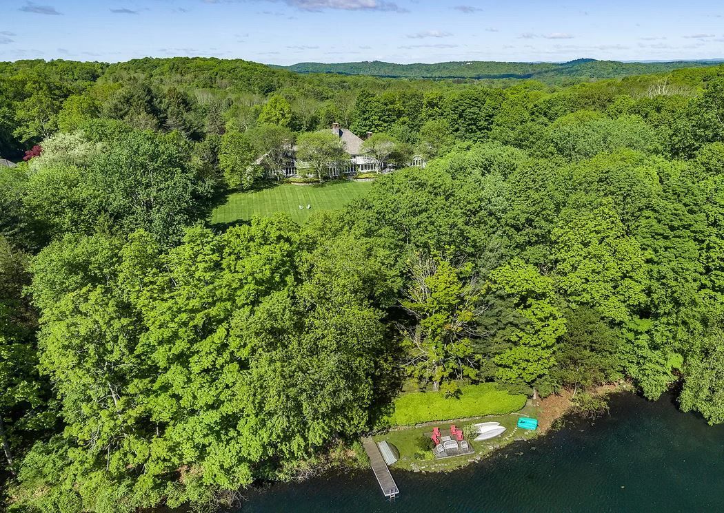 Aerial view of a home nestled in lush green trees next to a lake; small dock visible.