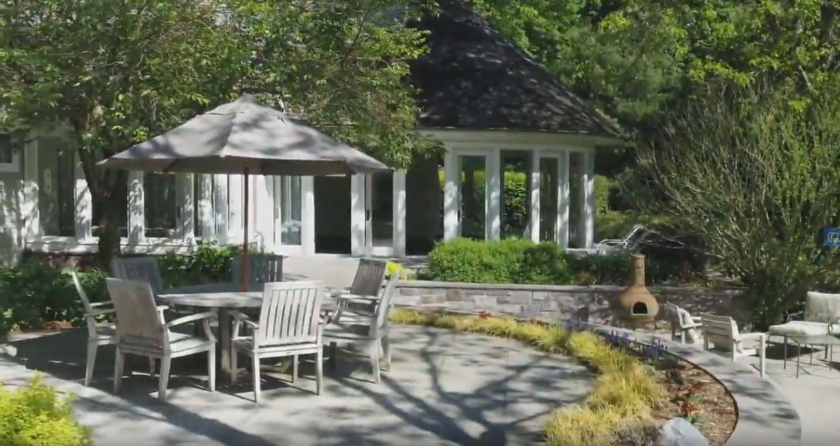 Patio with wooden furniture, gazebo, and lush landscaping. Sunny day.