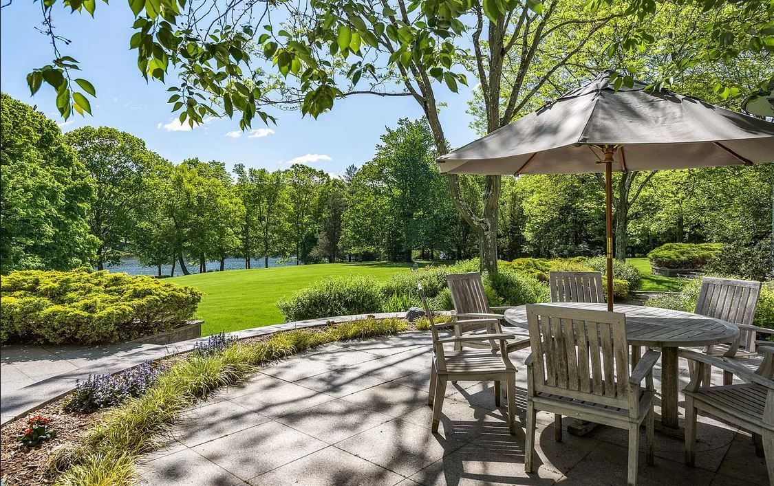 Patio with outdoor furniture, stone wall, grassy yard, trees, and lake view.