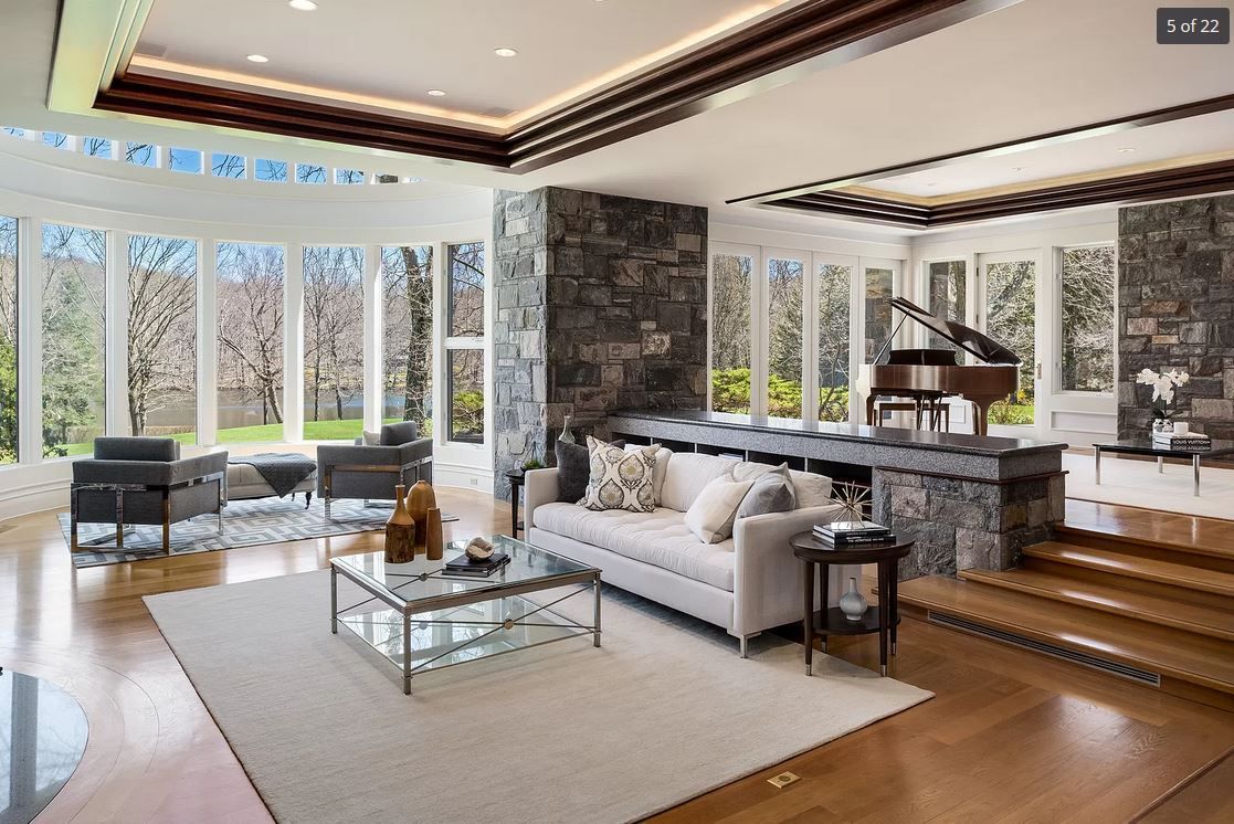 Luxurious living room with piano, stone walls, and large windows overlooking trees.