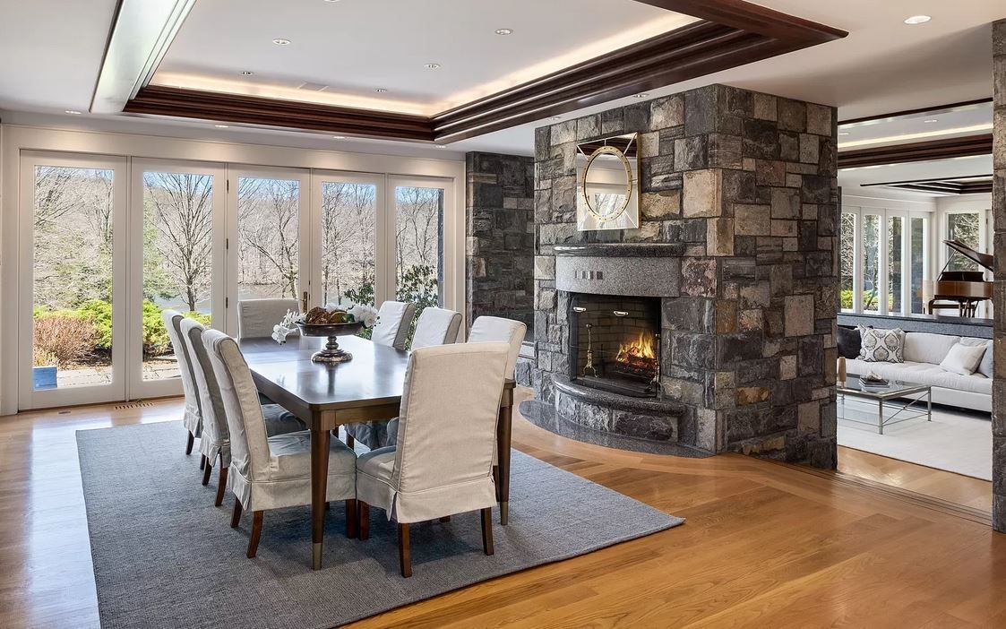 Dining room with stone fireplace, large table, and windowed walls.
