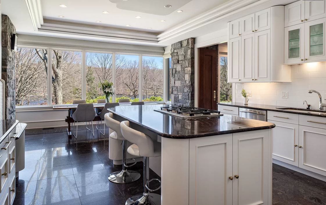 White kitchen with black granite island, large windows, and outdoor view.