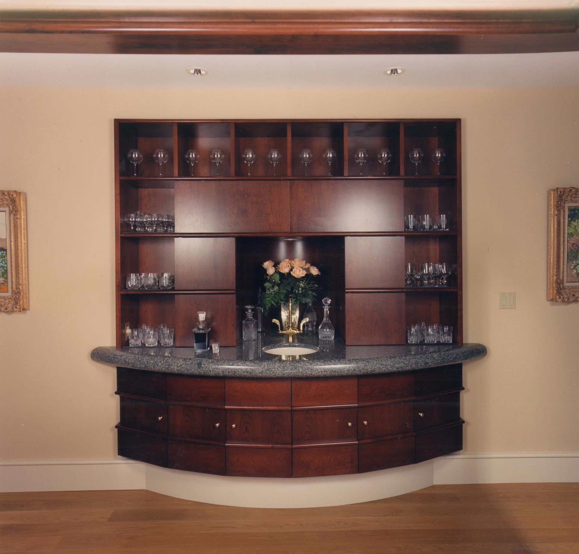 Built-in, dark wood bar with granite countertop, holding glassware and liquor bottles.
