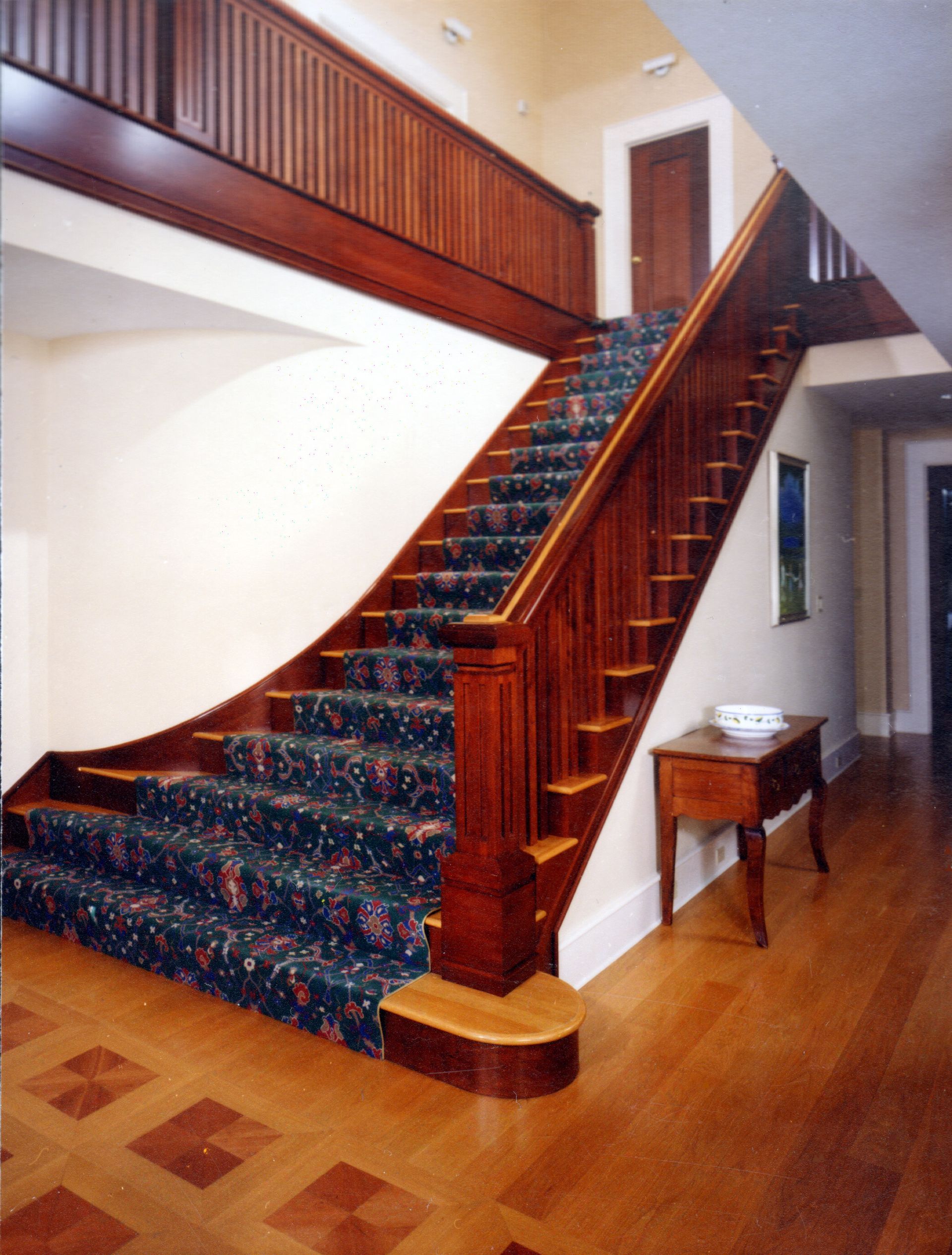 Wooden staircase with a patterned carpet and wooden railings in a foyer.