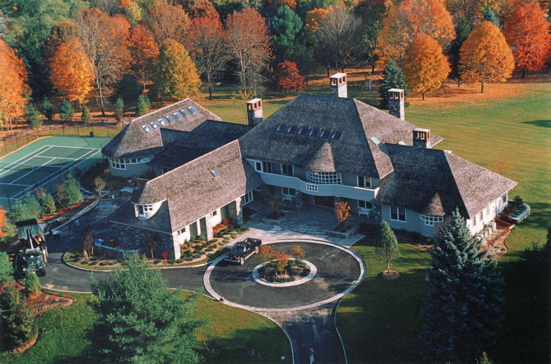 Large house with shingle roof and a circular driveway surrounded by fall foliage.