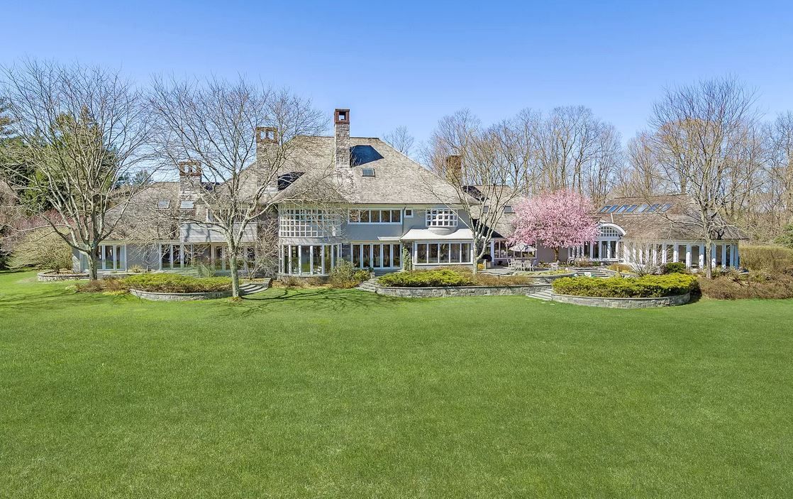Large, light-colored house with multiple windows and a gray roof sits on a green lawn.