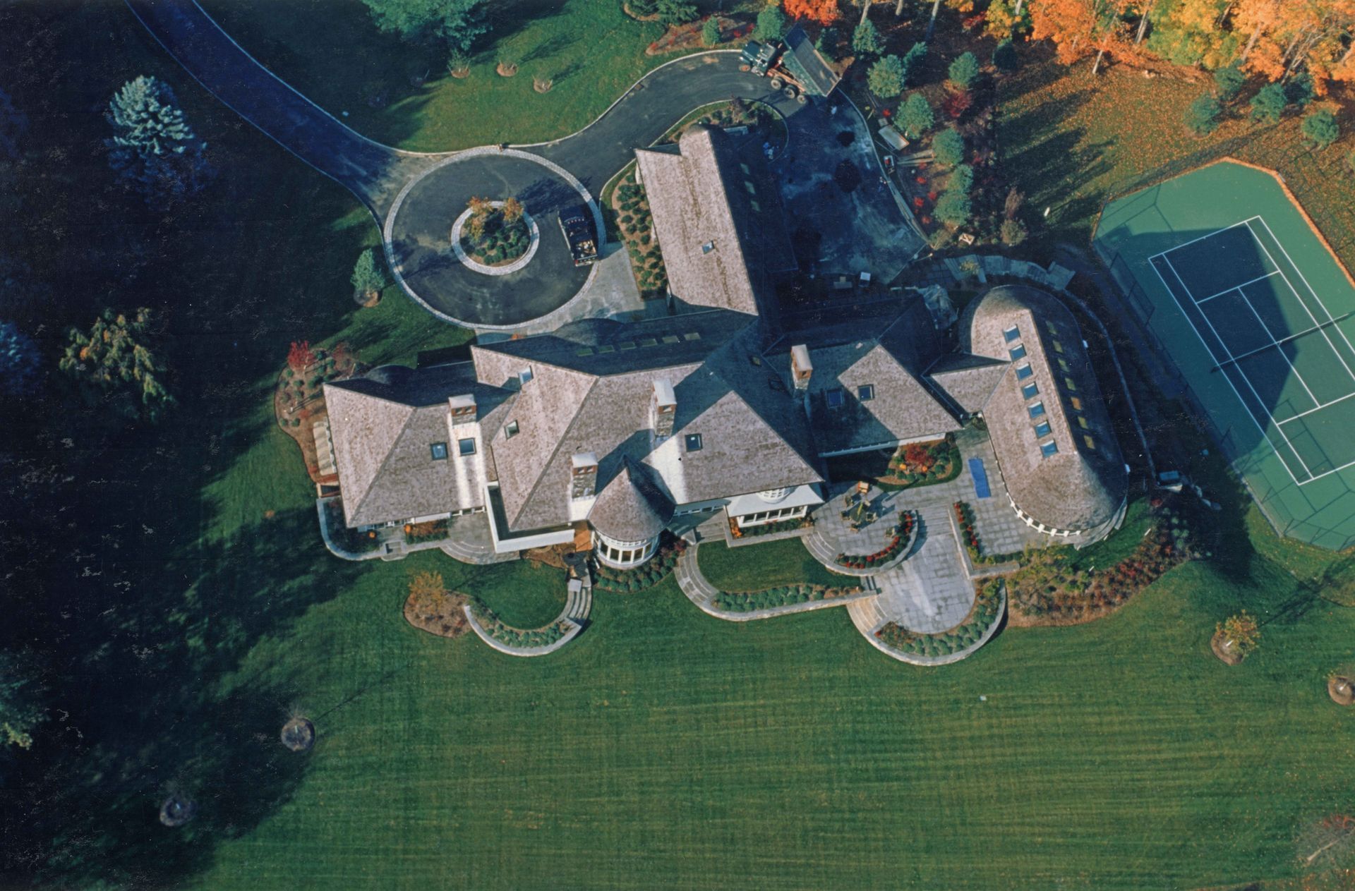 Aerial view of a large house with a circular driveway, tennis court, and manicured lawn.