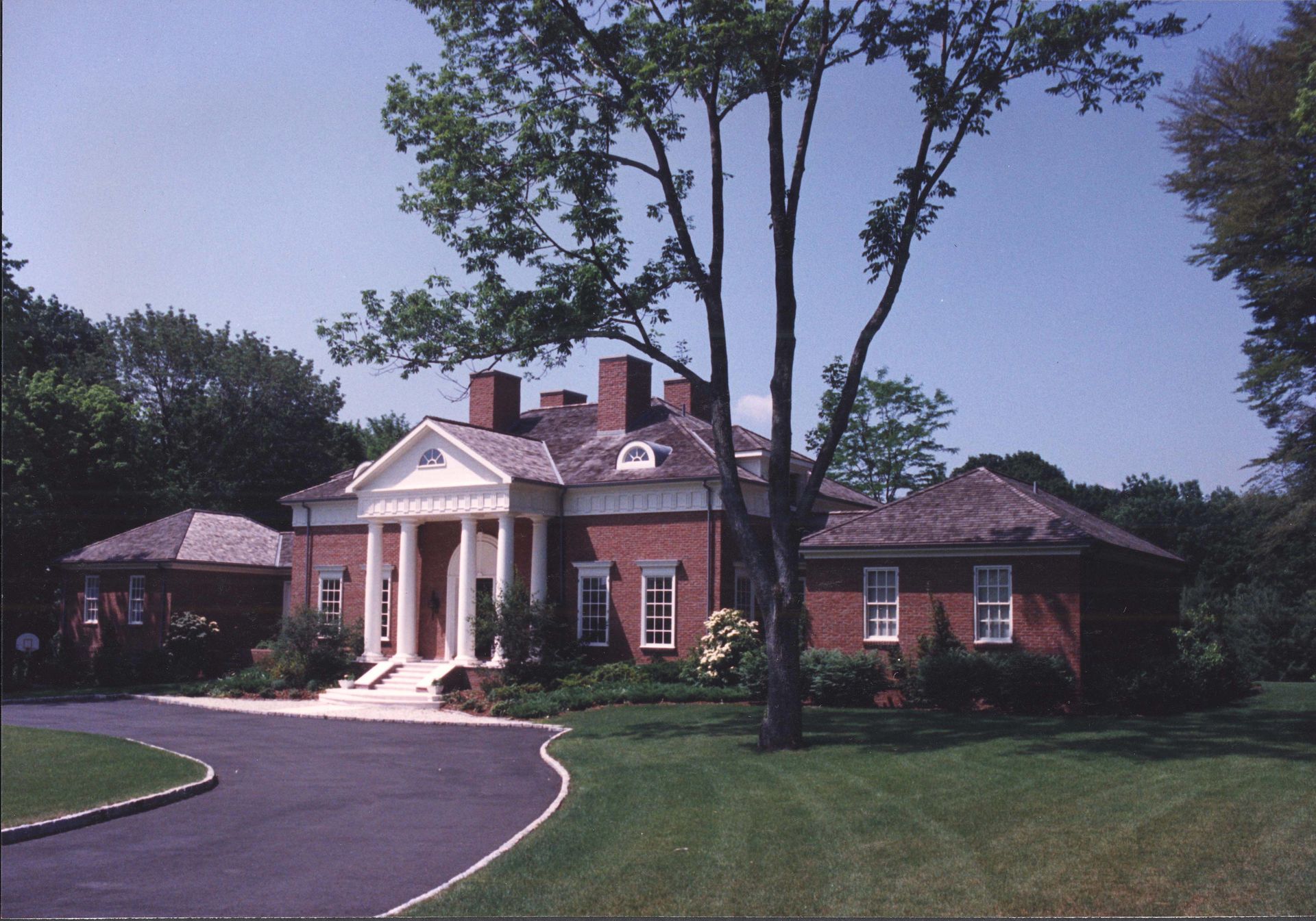 Brick mansion with white columns and green lawn, under a blue sky.