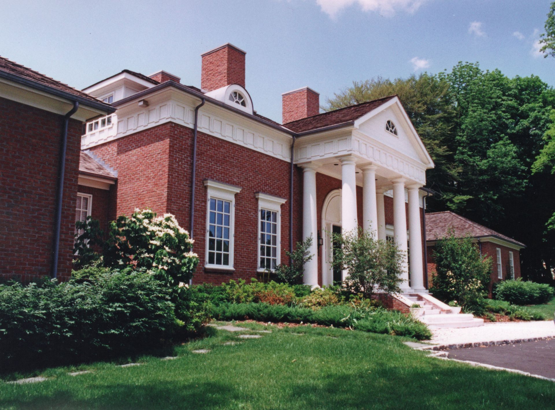 Red brick building with white columns and trim, green lawn, trees, and blue sky.