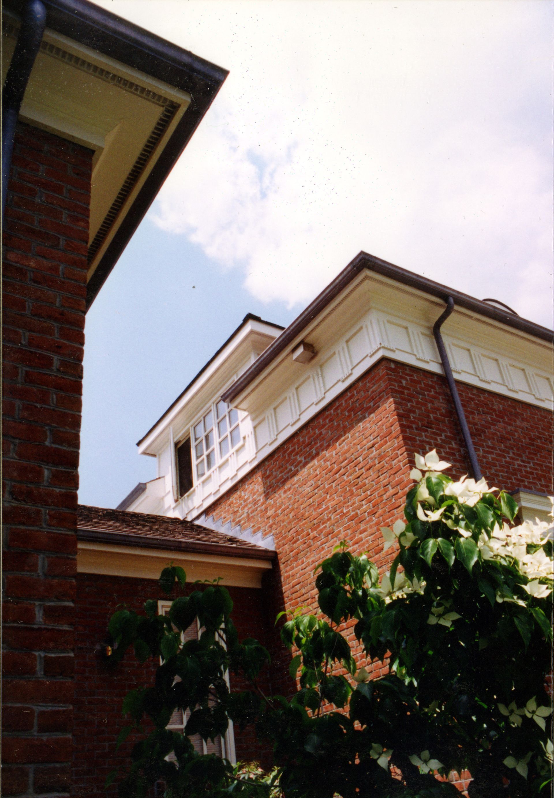 Brick buildings with white trim and a leafy tree against a partly cloudy sky.