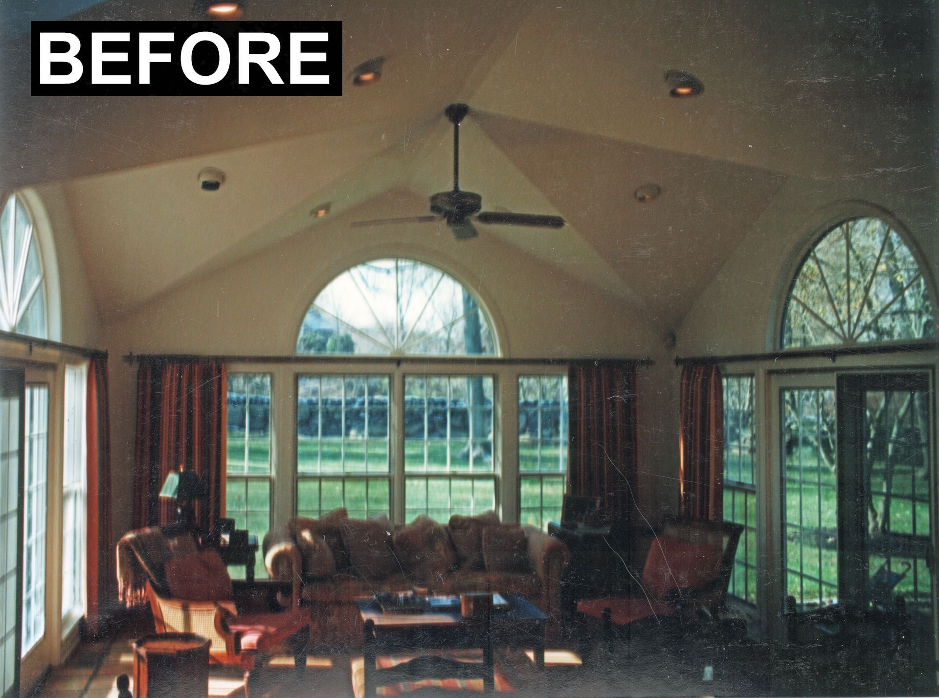 Sunroom before renovation, featuring arched windows, a sofa, and warm-toned curtains.