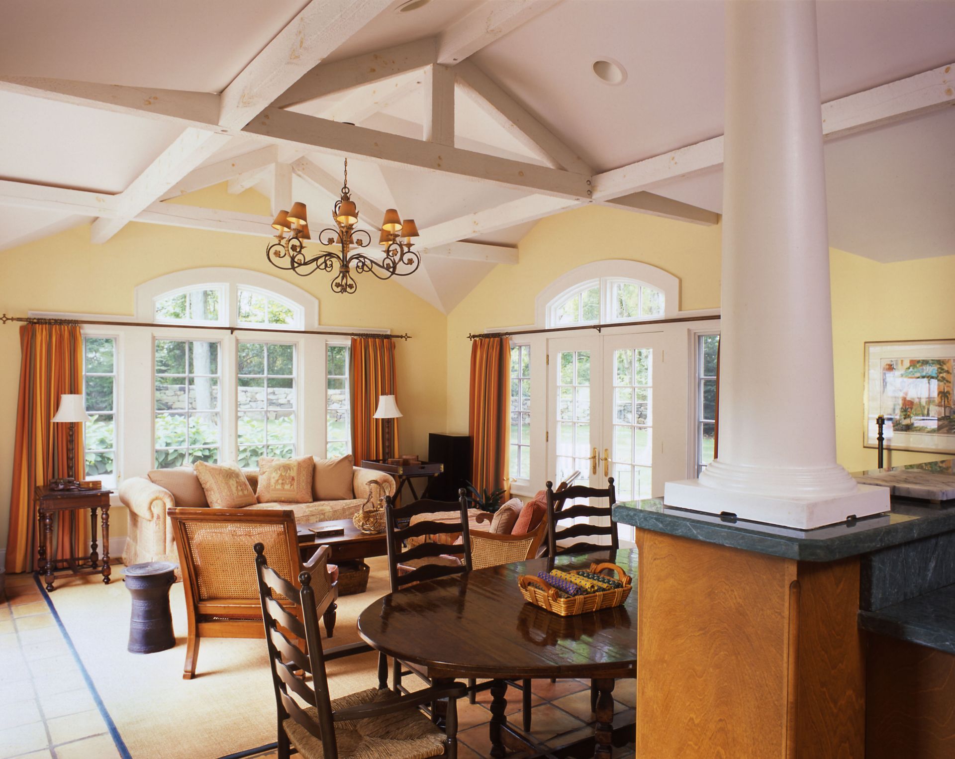 Living room with yellow walls, white beams, round table, and arched windows.