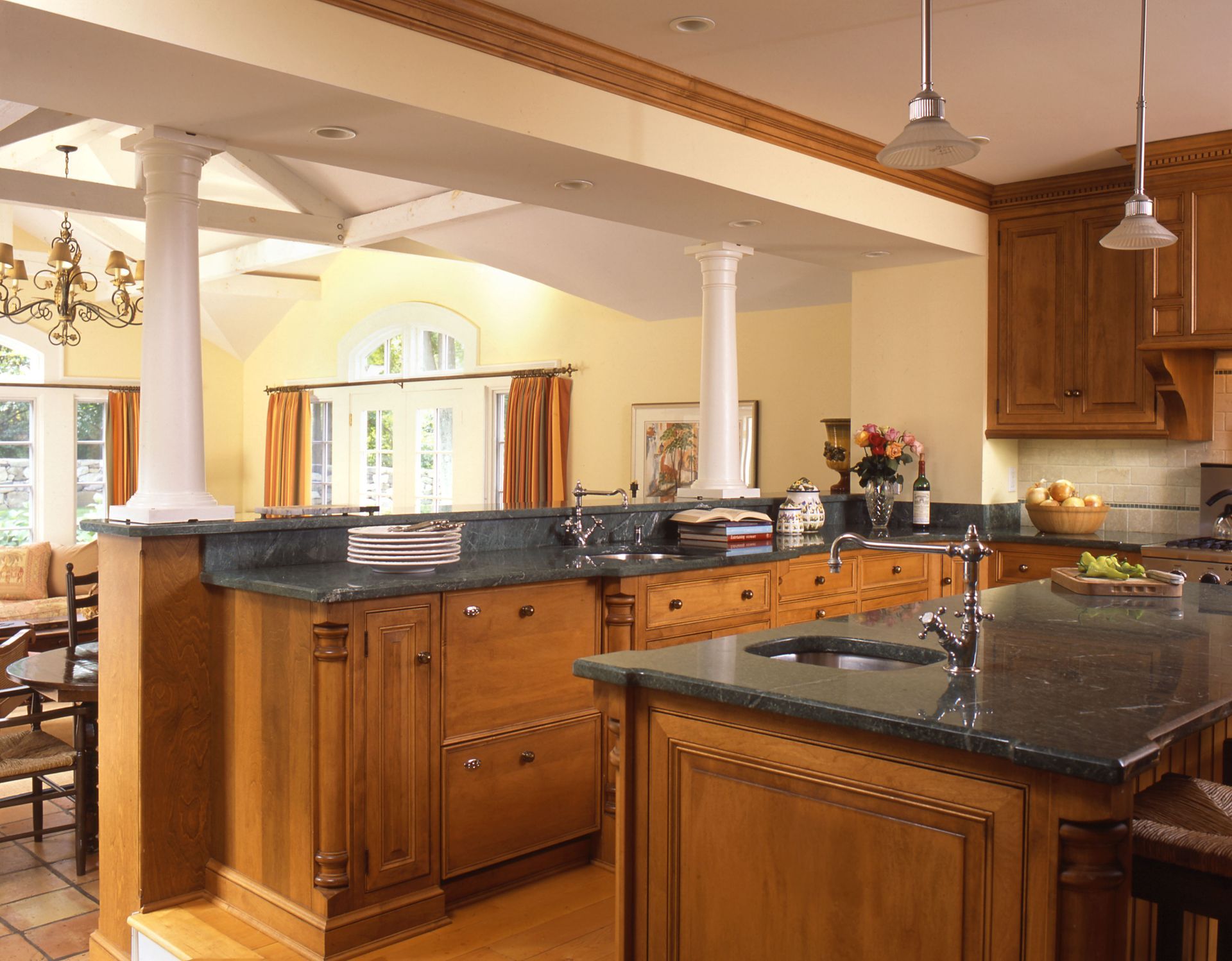 Kitchen with wood cabinets, green countertops, and two white columns separating it from a dining area.