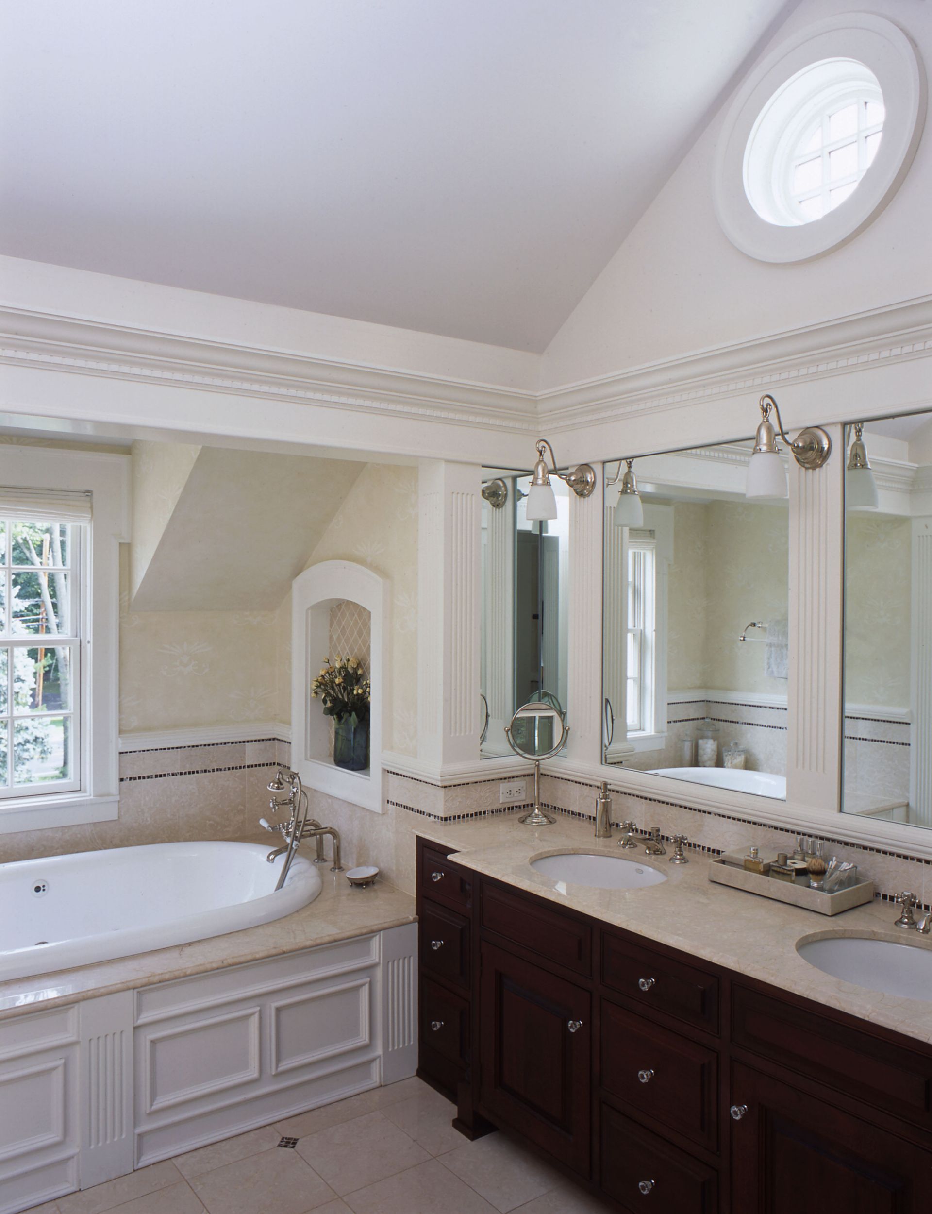 Elegant bathroom with a built-in tub, vanity with two sinks, and a small arched niche.