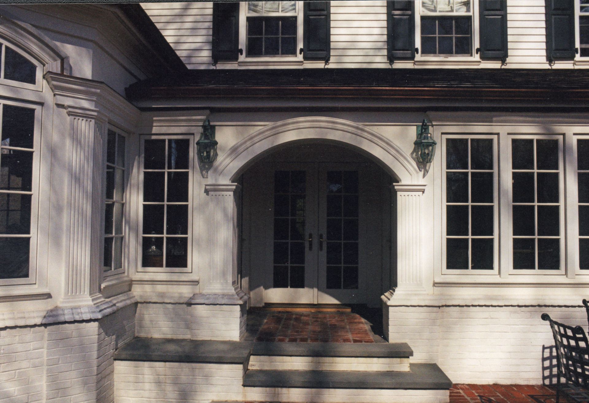 White house with arched doorway, windows, and steps leading to double doors.