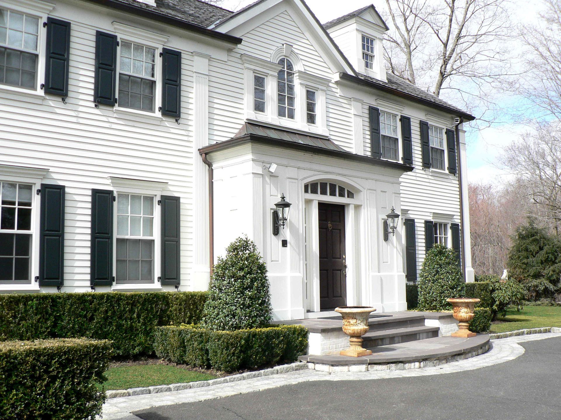White house with dark shutters, front entrance with stone steps, manicured landscaping.