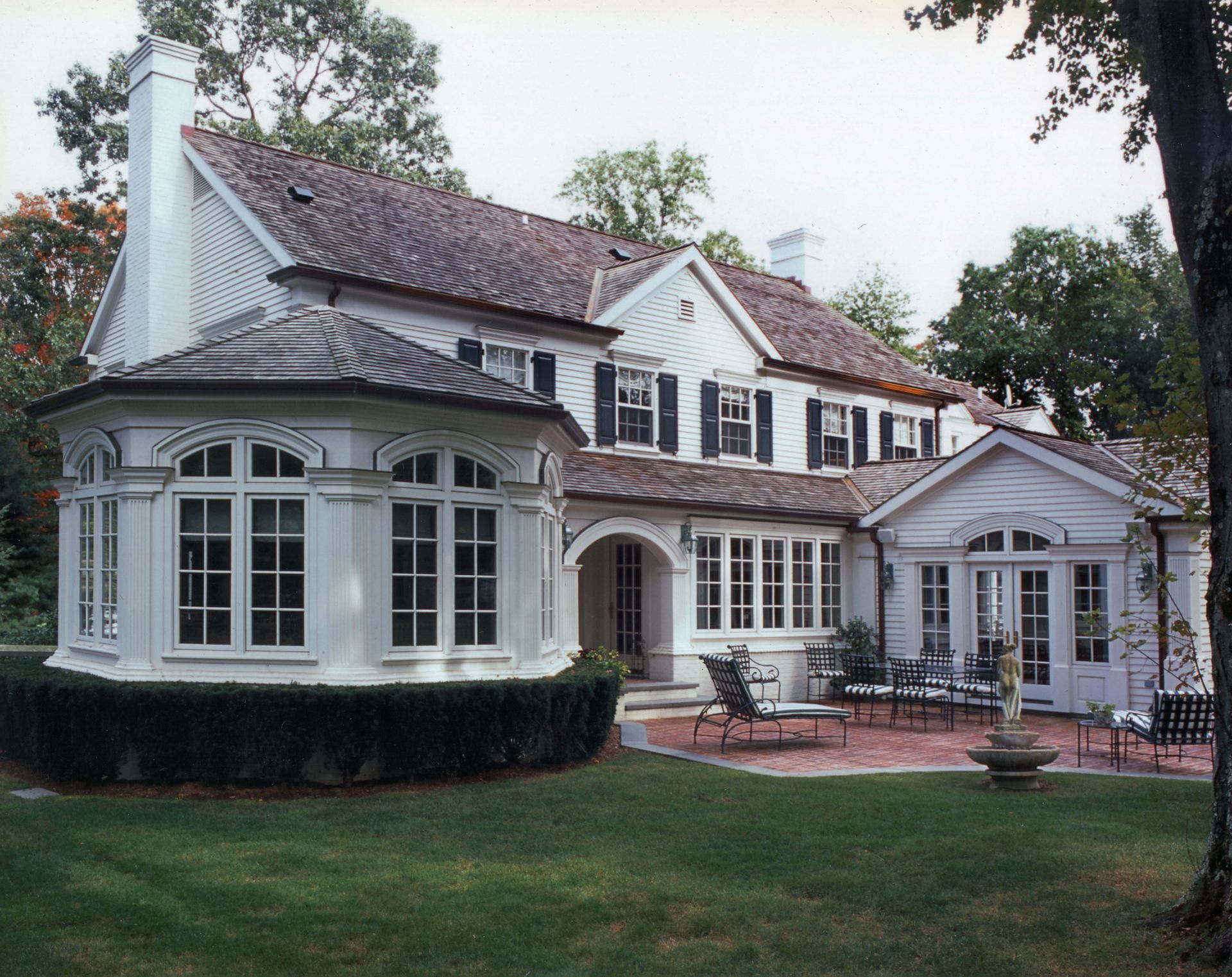 White two-story house with a brick patio, bay window, and a green lawn.
