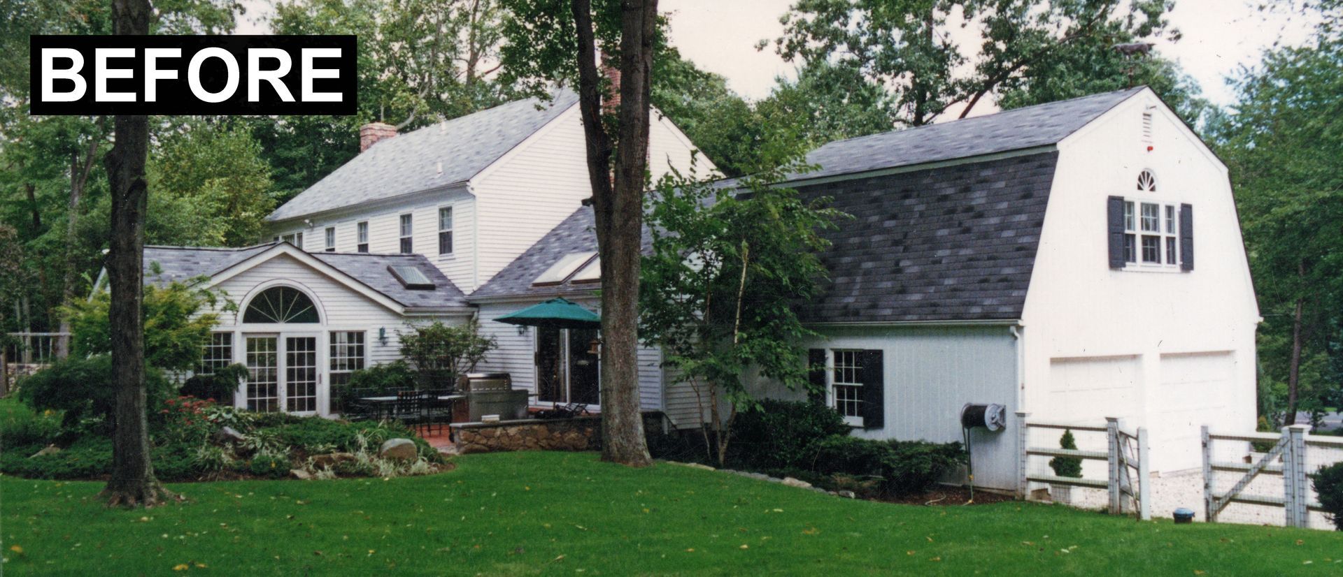 A white house with a barn-style garage. Green lawn, trees, and sky are visible. 
