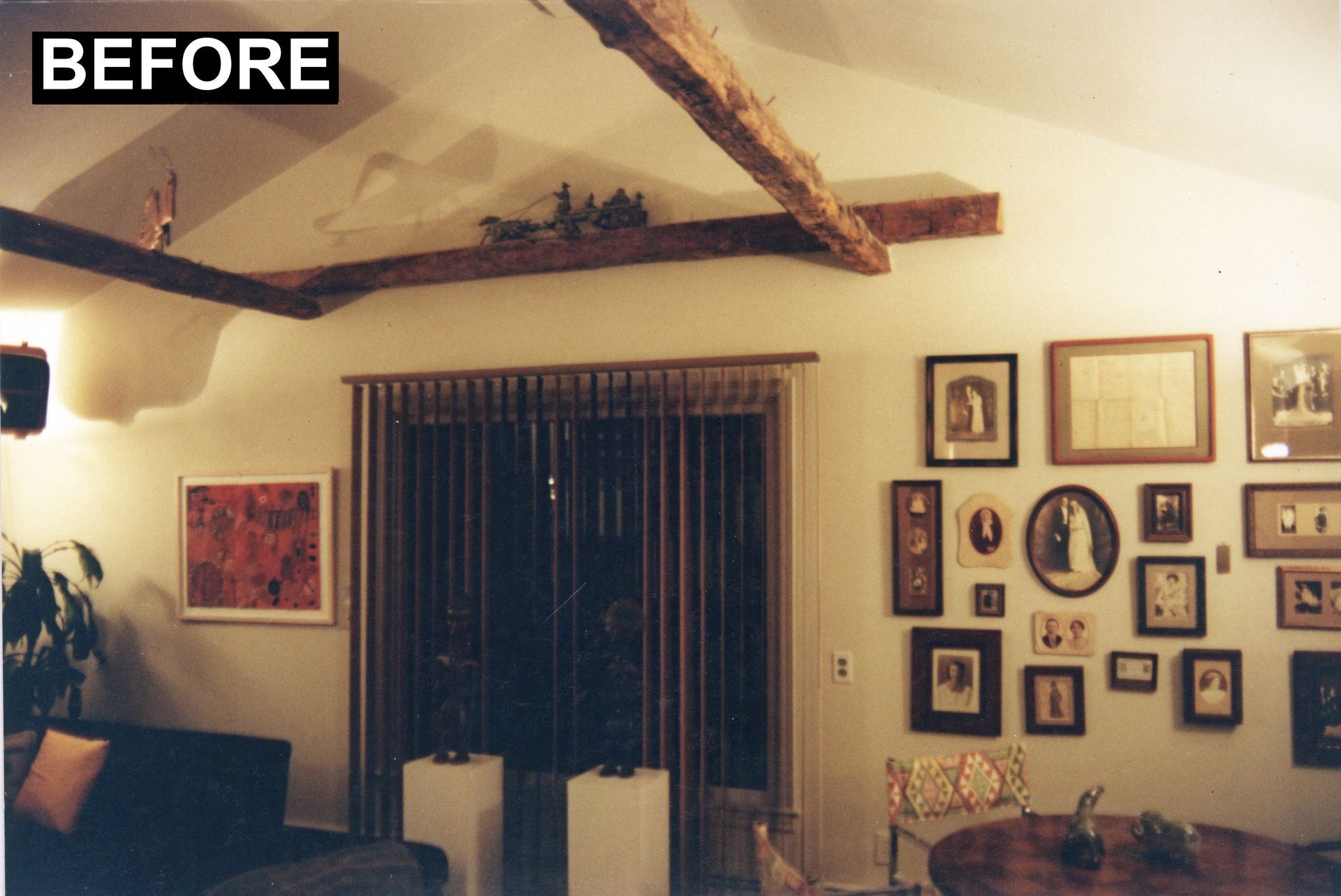 Living room before renovation with exposed beams, framed artwork, and a sliding glass door.