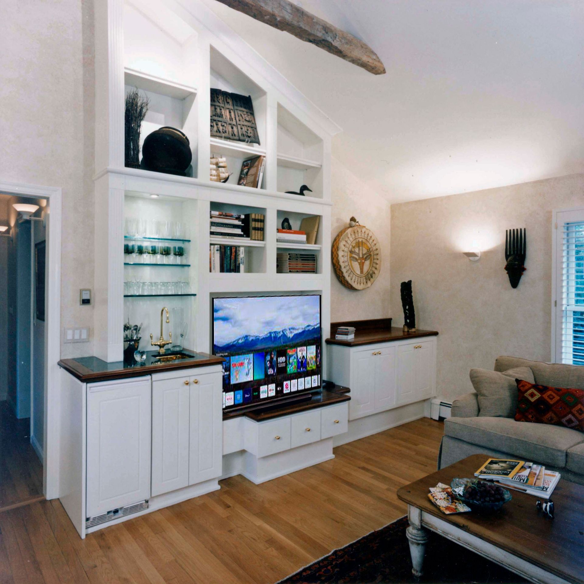 Living room with built-in white cabinets, TV, and shelves. Wooden floor and beige walls.