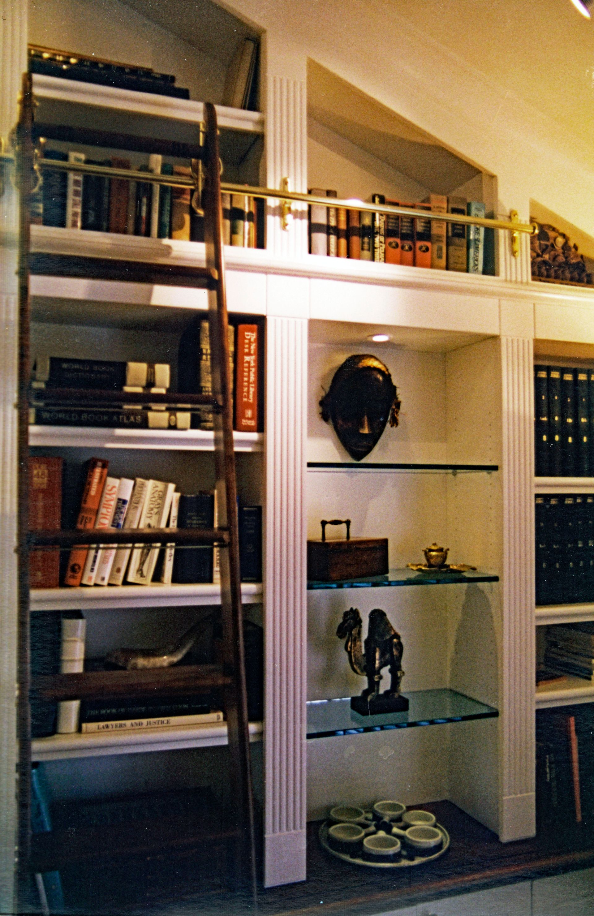 Bookshelves with a ladder. Books, decor, and a ladder are visible. White shelves, brass fixtures, and a wooden ladder.