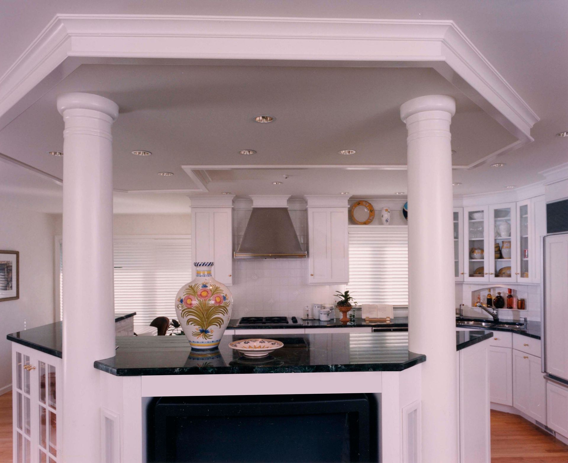 White kitchen with island featuring columns and black countertop. Bright, airy, and inviting.