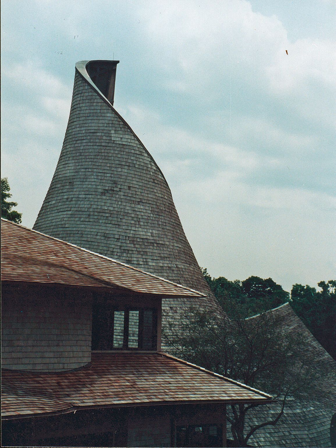 A tall, curved building with a textured roof against a cloudy sky.