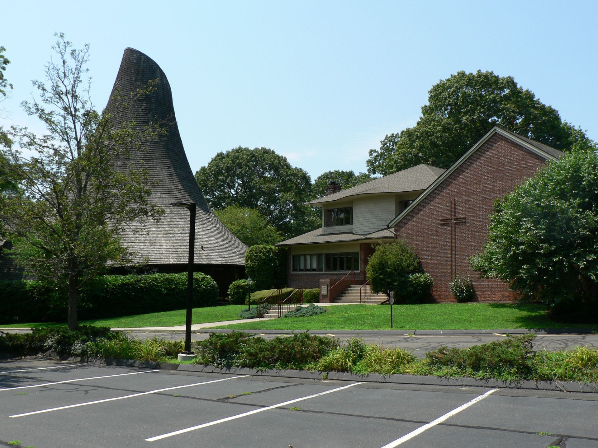 Church with distinctive conical roof, adjacent building, and parking lot.