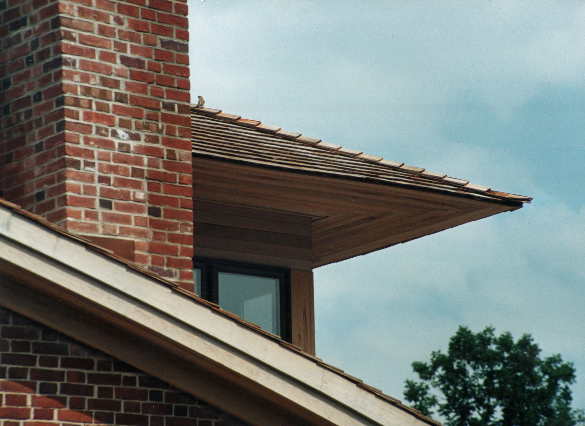 Brick chimney and wooden roof with a window, cloudy sky.