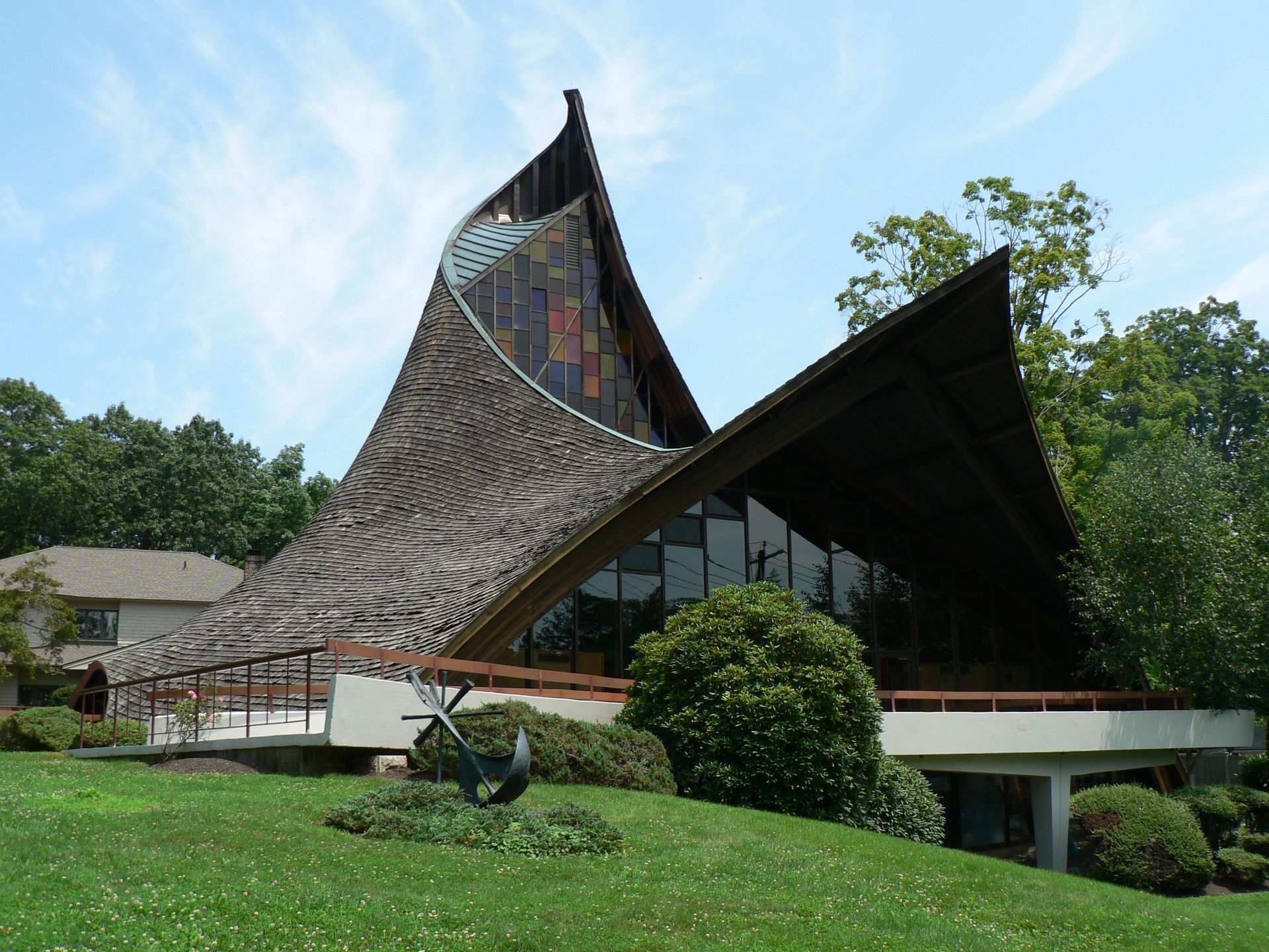 Modern church with a dramatically angled roof; glass windows, green lawn, and trees.
