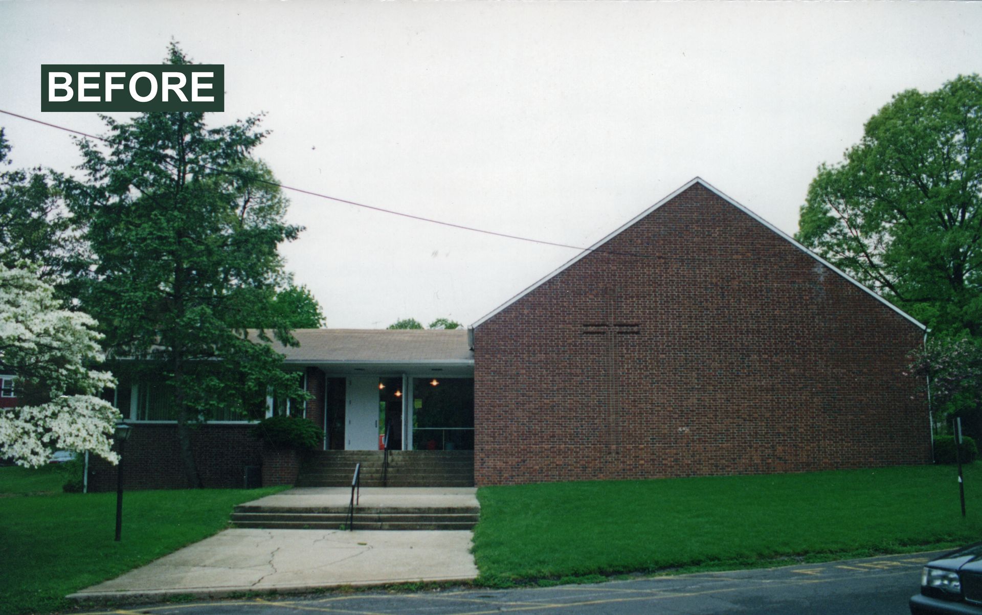 A brick building with a sloped roof. Green lawn and trees surround the building; gray sky.