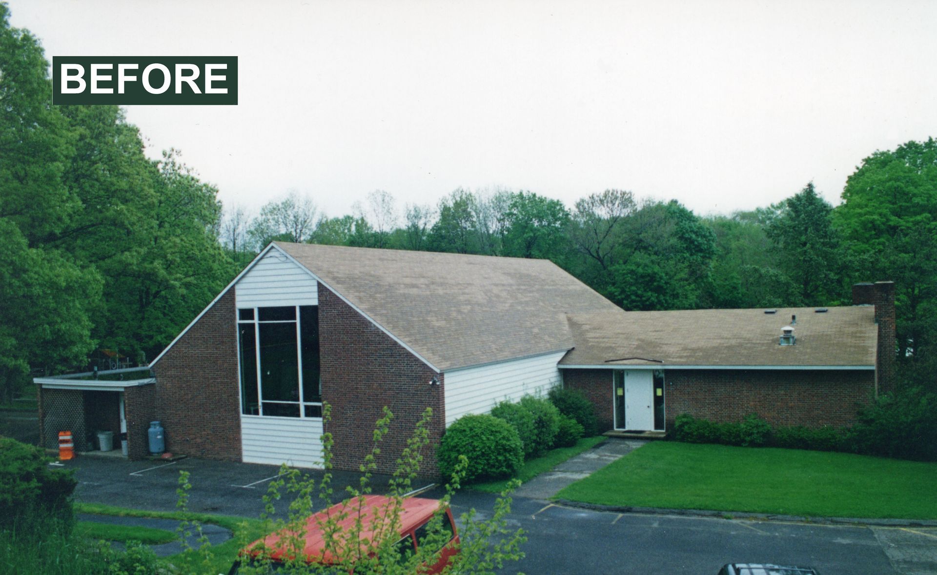 Exterior view of a church building with brown brick and tan roof, surrounded by green trees. 